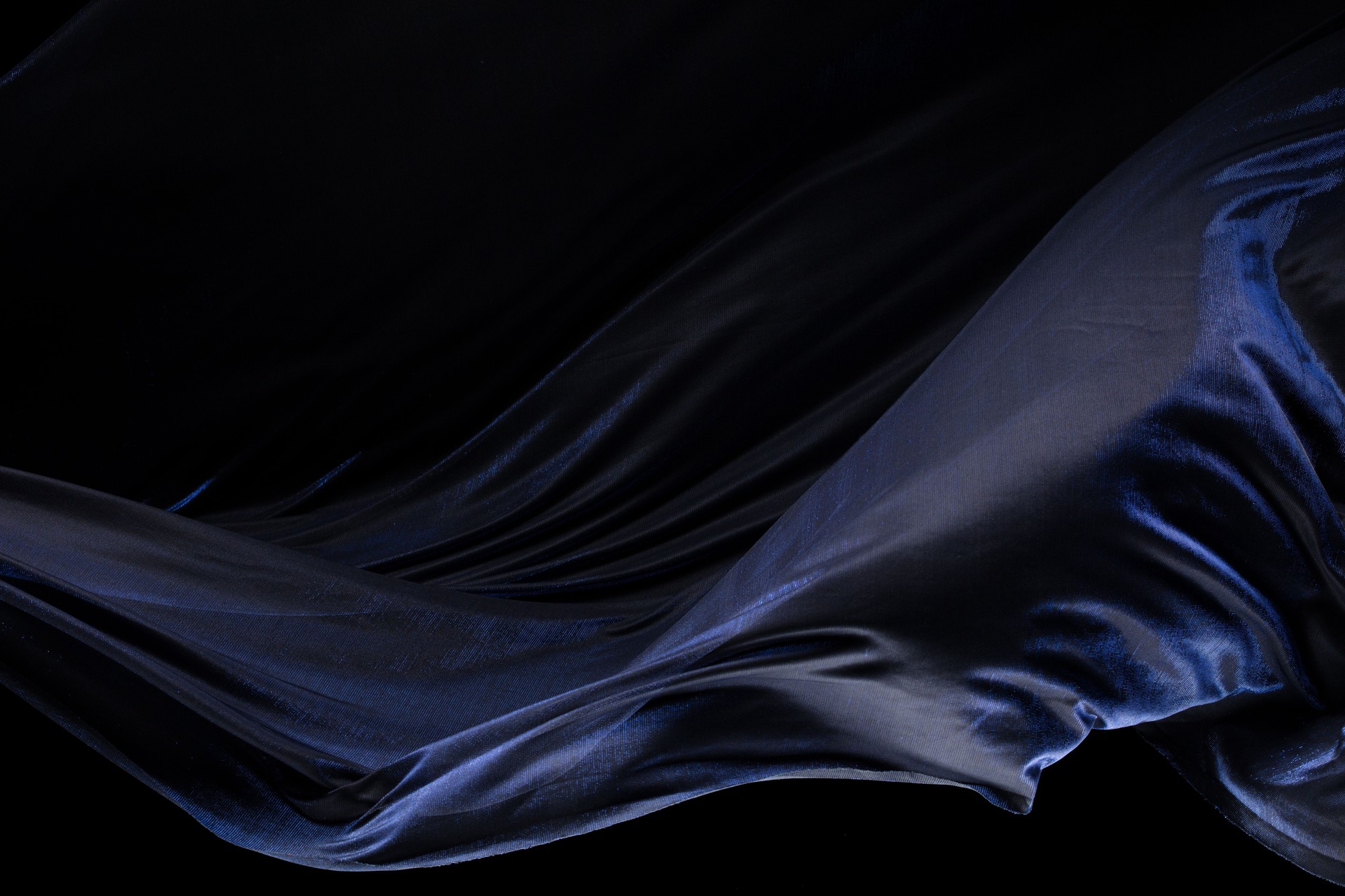 Blue silver shinny fabric flying in curve shape, Piece of textile blue silvery fabric throw fall in air. Black background isolated, dark shading environment